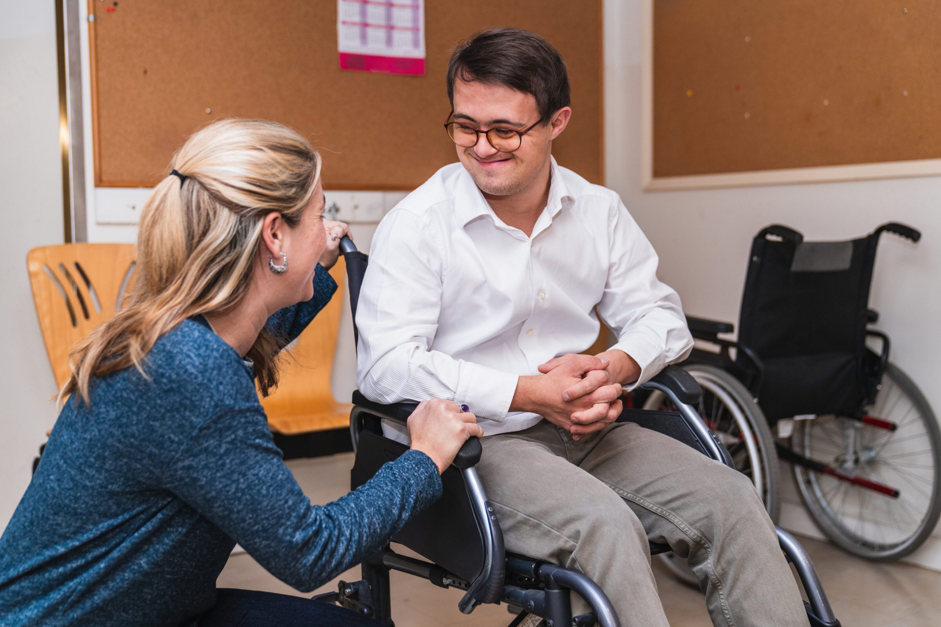 Empathetic Encounter: Woman Connects with Man in Wheelchair with Down Syndrome A heartfelt chat between a woman and a smiling man with Down Syndrome in a wheelchair.